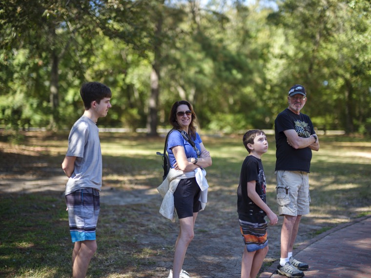 Four people standing together on a shaded lawn, mid-conversation.