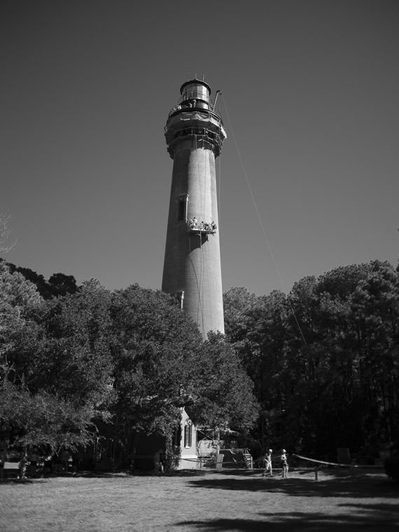 Black-and-white photo of the lighthouse against a clear sky, with tiny figures on the gallery near the top.