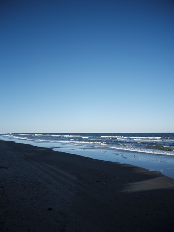 Beach in late afternoon light, wet sand reflecting the sky and waves rolling in.