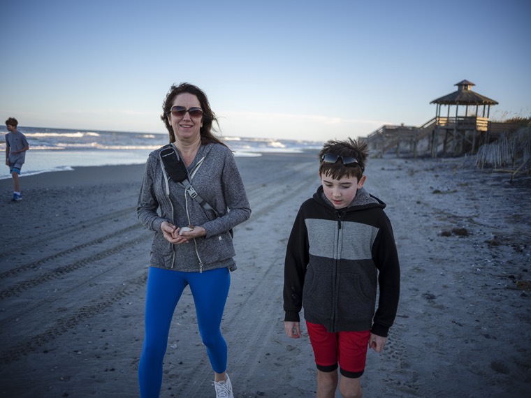 Two people walking along the beach toward the camera, a third far off near the waves, a gazebo in the distance.